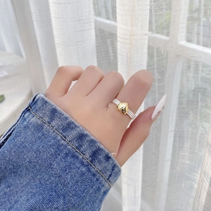 Close-up of 925 silver twist ring with gold heart on model finger in casual setting