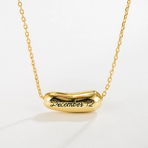 Detail of gold capsule pendant with December 12 engraving on minimalist chain