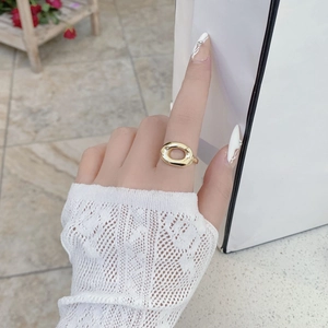 Détail d'une bague dorée ovale ajourée portée sur un poignet en maille blanche