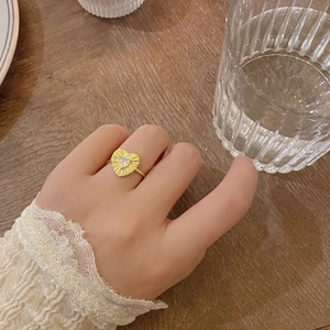 Detailed view of a gold heart ring with pleated texture and zircon worn by a model