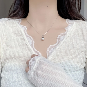 Close-up of S925 silver necklace with a white baroque pearl pendant on a lace dress