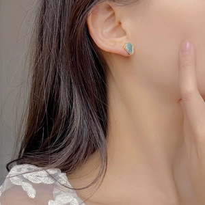 Macro shot of minimalist gold hexagonal stud earrings with grey shell inlay on the ear