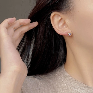 Nahaufnahme eines herzförmigen lila Zirkon-Ohrrings mit Vergoldung, getragen von Model
