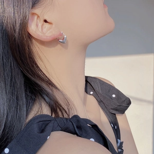 Polished silver puffed heart hoop earring shown on a female model in a lifestyle setting