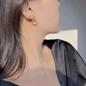 Close-up of heart-shaped twisted gold earrings on a model in minimalist black attire