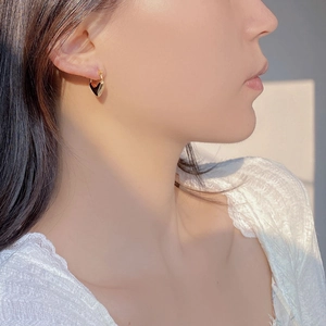 Close-up of elegant gold heart hoop earrings worn by a model in natural sunlight