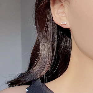 Close-up of three graduated pearls set on silver stud earrings worn on the earlobe