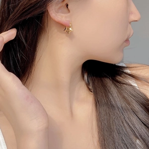 Close-up of a minimalist gold star earring worn on the earlobe with smooth 3D design