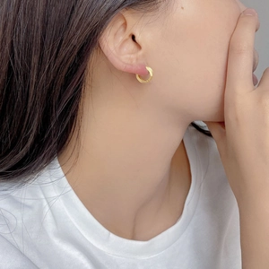 Detail of matte brushed gold 925 sterling silver hoop earring worn on female model's ear