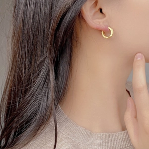 Close-up of golden brushed metal hoop earrings worn by a model in soft lighting