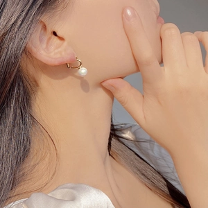 Close-up of a model wearing a gold heart earring with a dangling white pearl