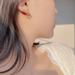 Close-up of minimalist gold huggie hoop earring with a clear gemstone on an elegant model
