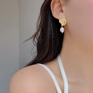 Close-up of gold lava texture earrings with white baroque pearls worn on model