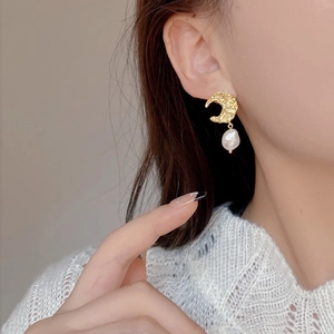 Macro detail of moon-shaped hammered gold earring featuring a baroque pearl drop on model