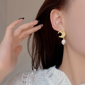 Detail of gold textured moon earring with a baroque pearl on a female model