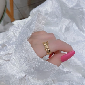 Elegant gold bubble letter ring on finger with white lace cuff in a soft lifestyle setting