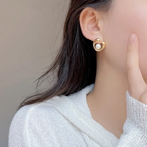 Close-up of a model wearing gold swirl earrings with natural freshwater pearls