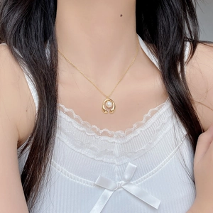 Dettaglio di una collana dorata con ciondolo a perla curva indossata da una modella
