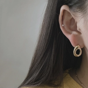 Detailed view of polished gold oval hollow earrings and matching stud on ear