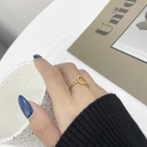 Minimalist gold hollow circular ring on a hand touching a ceramic cup in lifestyle view
