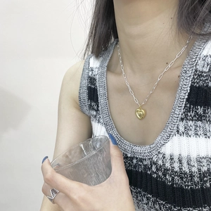 Gros plan d'un collier en argent 925 avec pendentif cœur doré 3D porté par un modèle