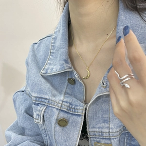 Detail of gold crescent moon necklace and silver snake ring on a model in denim