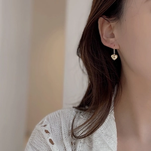 Detail of a textured golden heart earring worn by a model in warm light settings