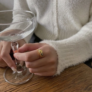 Close-up of minimalist gold-plated dome ring worn on a finger holding a glass