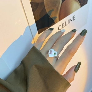 Détail d'une bague coeur en argent 925 avec pierres roses et vertes sur une veste olive