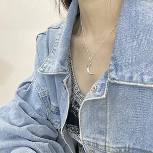 Detail of silver crescent moon necklace with embossed texture on woman's collarbone