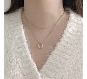 Macro view of gold-layered necklace featuring a sleek circle pendant on a knitted sweater
