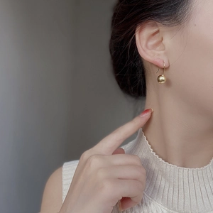 Close-up of a minimalist golden ball drop earring worn by a model with polished finish