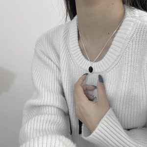 Dettaglio del ciondolo ovale in smalto nero argento S925 su un modello con maglia bianca