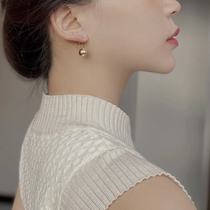 Close-up of minimalist gold spherical drop earring on model with polished mirror finish