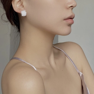 Macro detail of square woven texture silver stud earrings worn on female model's ear