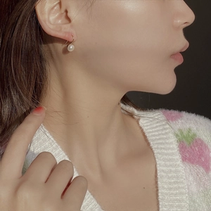 Close-up of elegant S-shaped gold earrings with high-luster natural freshwater pearls