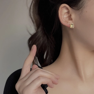 Close-up of elegant gold square stud earring showing a polished finish on model's ear