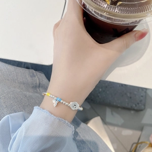 Detail of silver beaded bracelet with rainbow and cloud charms worn by hand