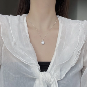 Close-up of S925 silver necklace with oval coin pendant on elegant white blouse
