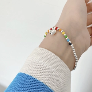 Detailed view of rainbow beaded bracelet with silver heart pendant on wrist