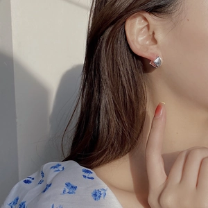 Close-up of a silver geometric cube stud earring on ear with polished finish