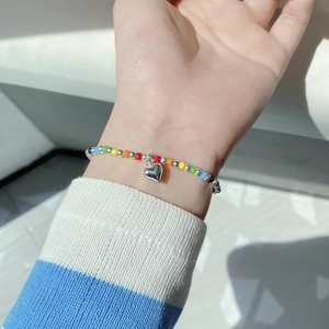 Detail of colorful rainbow beads and silver heart charm on an elastic cord bracelet