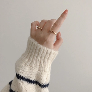 Close-up of minimalist wave pattern gold rings worn on fingers with a cozy knit sweater