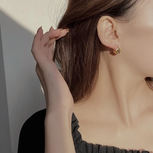 Close-up of minimalist gold twisted geometric earrings worn by a model in natural light