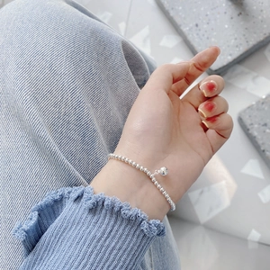 Close-up of minimalist 925 sterling silver beaded bracelet with a small bell charm on wrist