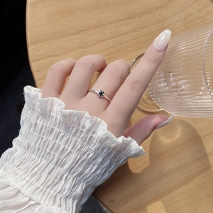 Detail of silver clover ring with black flower on hand by a glass of water