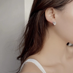 Detail of a minimalist silver heart-shaped earring worn on the ear for a stylish look