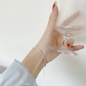 Close-up of minimalist 925 sterling silver box chain bracelet worn by a model holding a glass