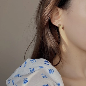 Close-up of golden heart earrings with hammered texture worn on female ear lobe