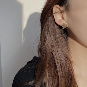 Macro shot of gold geometric earrings with vertical wave texture on female model